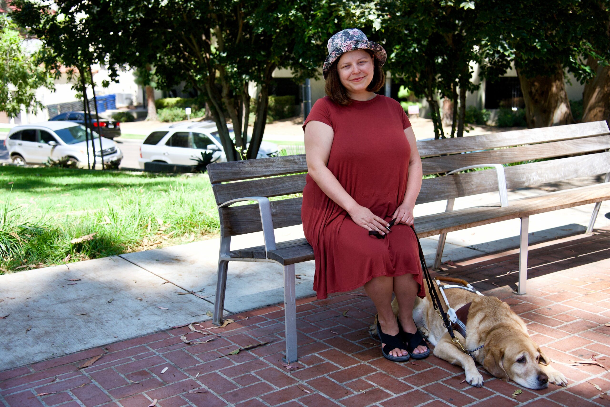 A woman sits in the park with her dog. She poses demurely towards the camera and smiles while her dog takes refuge from the sun on the shaded ground. It is a familiar image, not dissimilar to a thousand family snaps.