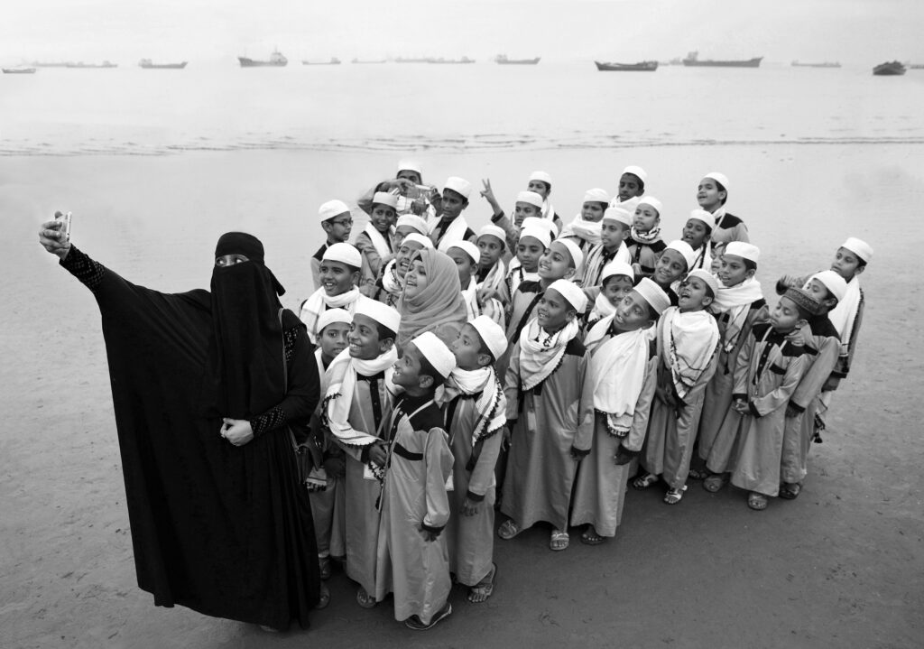 A school teacher leads her students on a tour and takes a collective selfie of them standing together by the seashore.