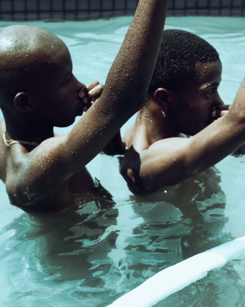 Two men stand closely in a pool during a hot summers day.