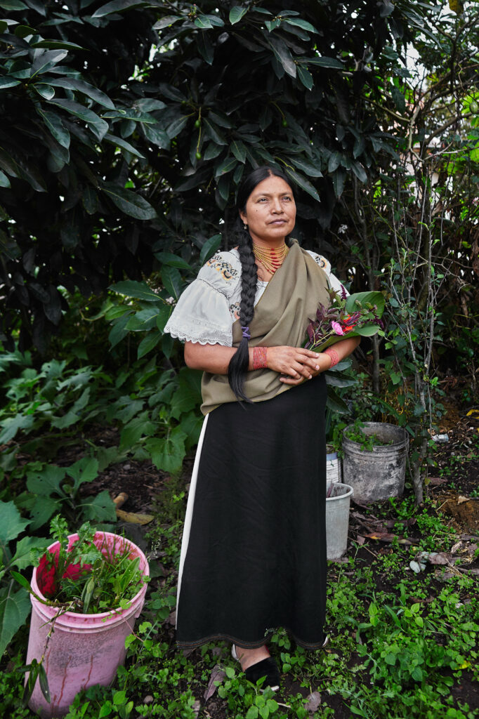 Martha Arotingo serenely poses for a portrait in the lushness of her garden. In her arms, she cradles a colourful bouquet of plants and flowers.