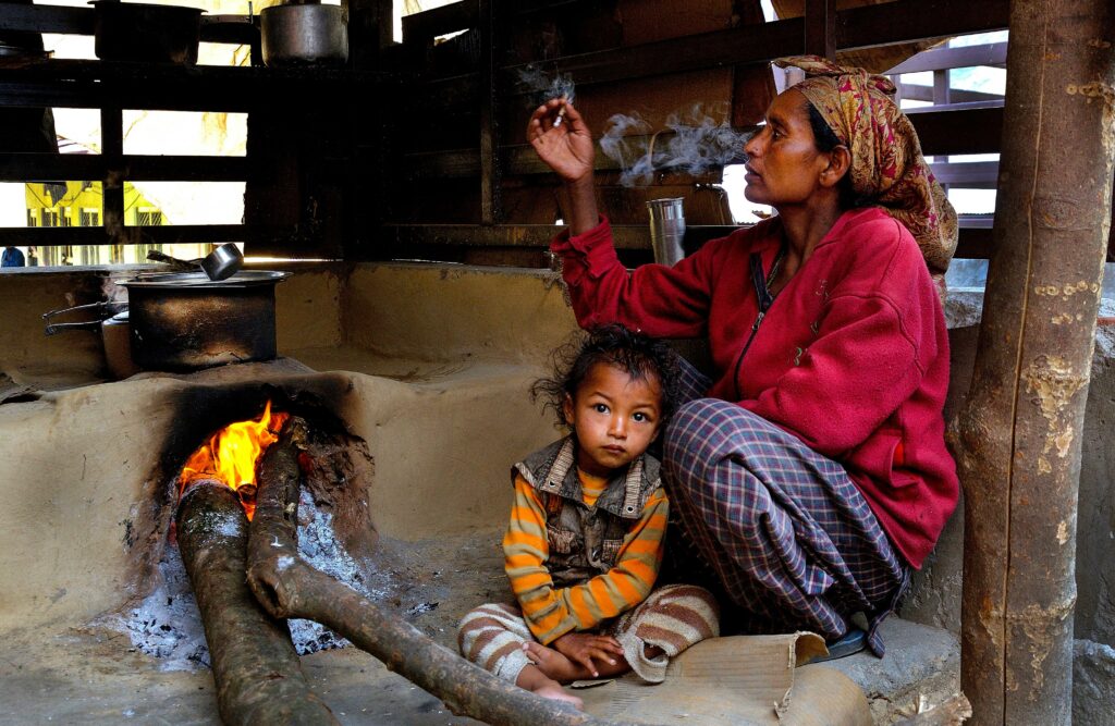 A woman smokes a cigarette next to her child in a small mud hut kitchen in the village of Taluka, Uttarakhand, India.