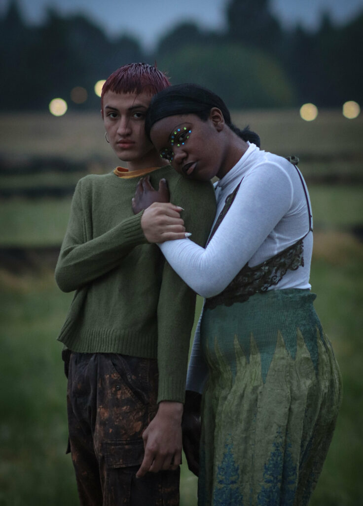 Two houseless transgender teenagers hold each other in a field.