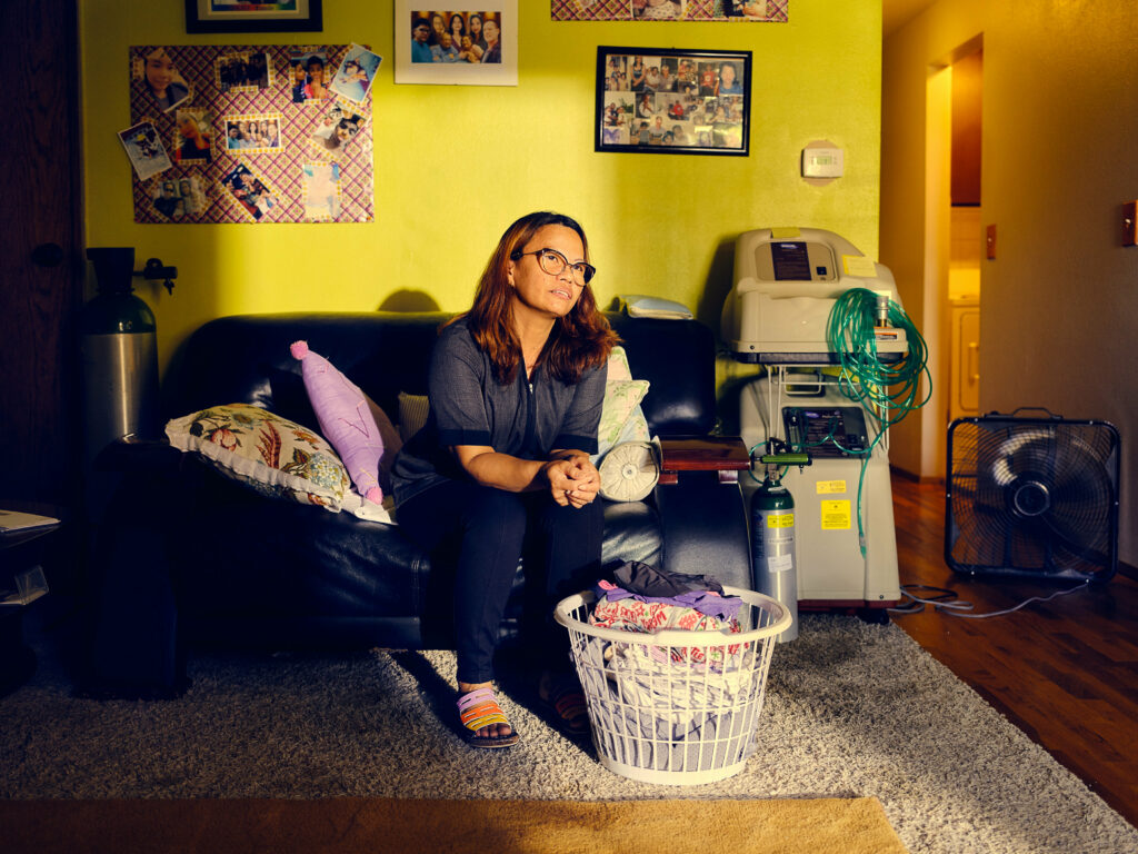 Hotel housekeeper Liza Cruz, age 42, poses for a portrait at her home with a pile of laundry in front of her.