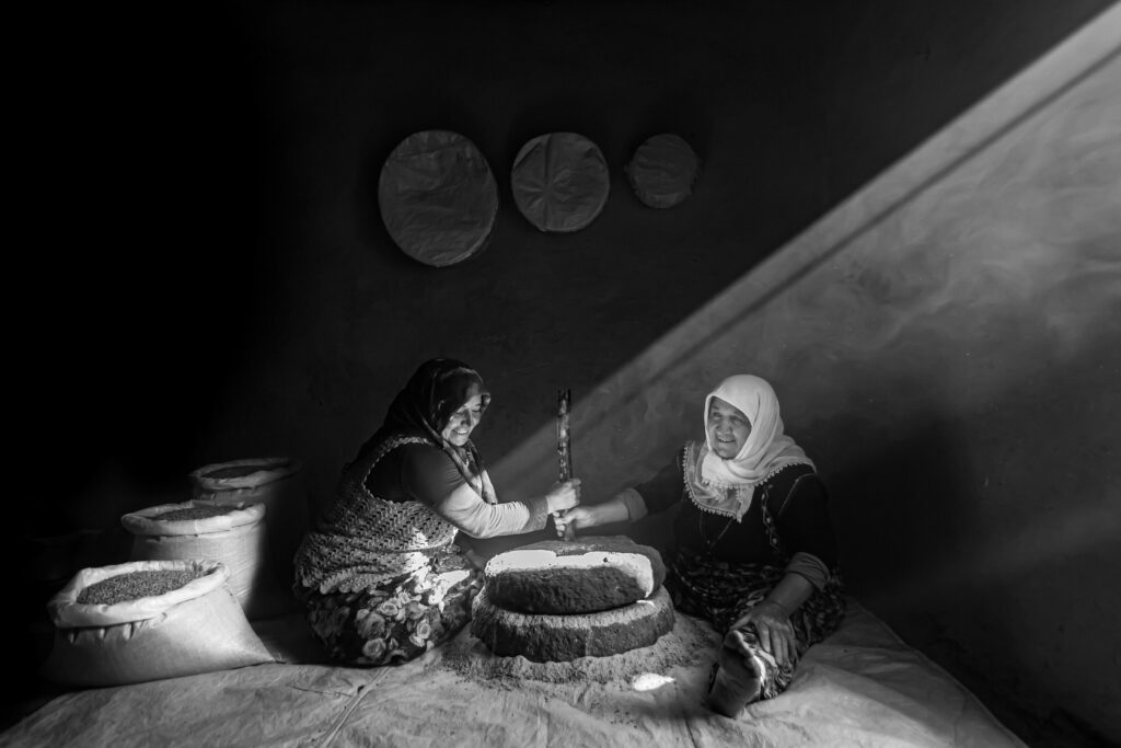 Two women grind green lentils on a hand mill in a village in Turkey.