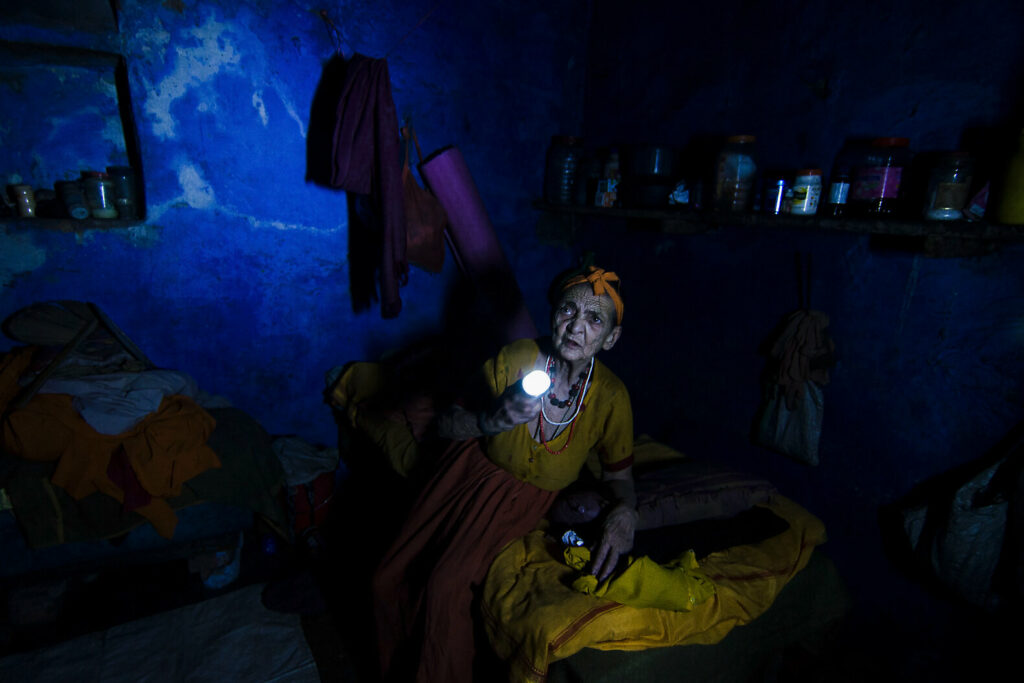 In the midst of a power cut, an elderly woman searches for her medicines. The small room is shrouded in darkness, lit only by the bright white light of the woman’s torch that radiates outward exposing the cracked wall, the makeshift shelf and piles of clothes.