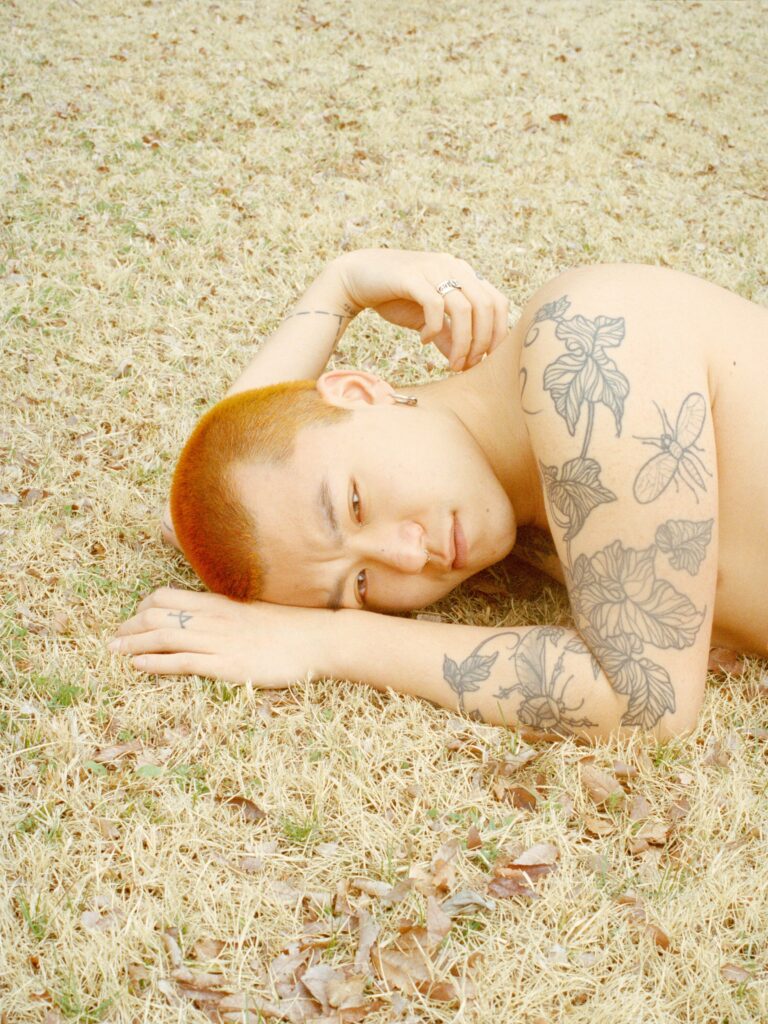 A young man lies on yellow grass. He seems pensive, relaxed amongst the muted colour of the faded grass.