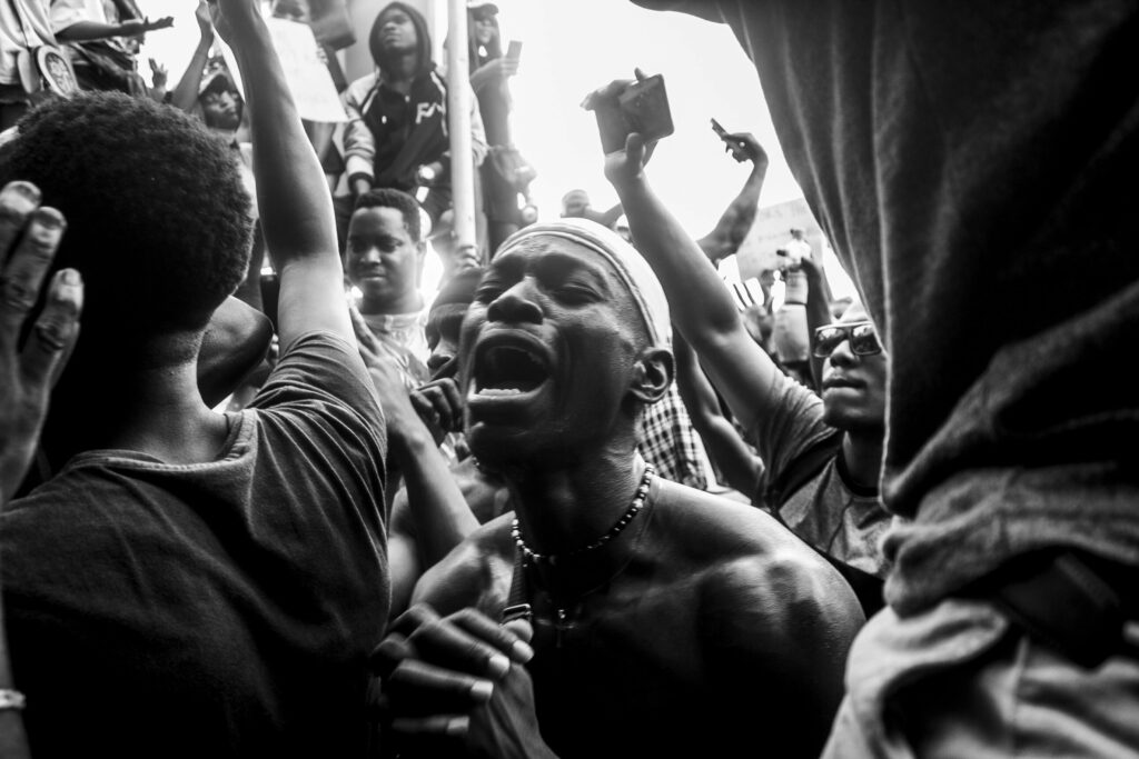 A man screams, hands clasped, eyes closed. Around him others wave signs to protest police brutality and demand the disbandment of the Special Anti-Robbery Squad, a notorious unit of the Nigerian Police with a long record of abuses.